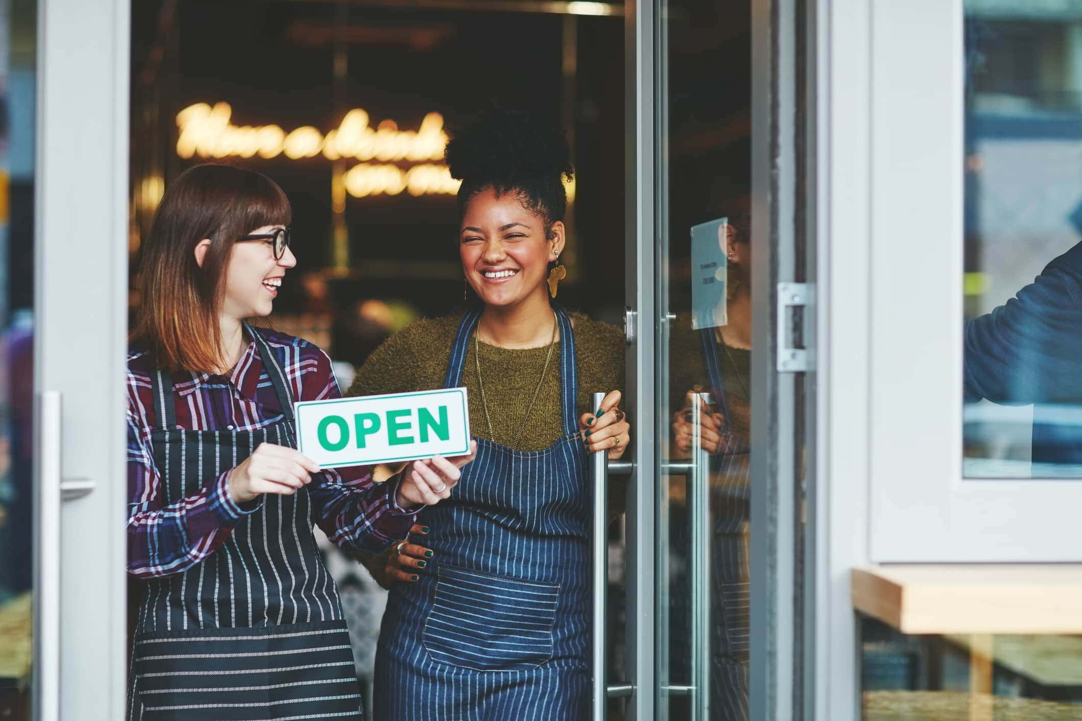 Two young women holding up an open sign in their coffee shop