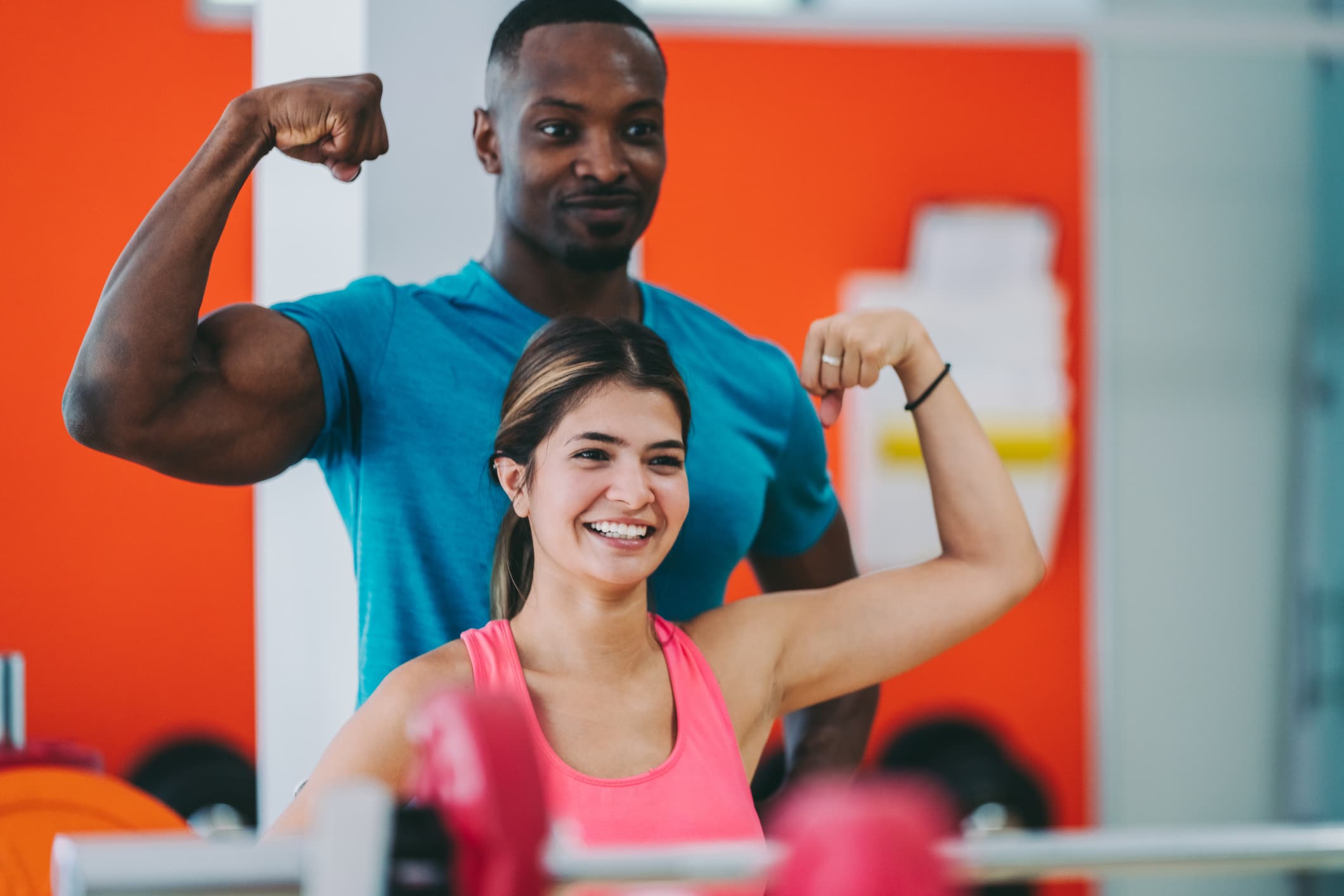 Smiling couple flexing biceps in front of the mirror in gym after workout