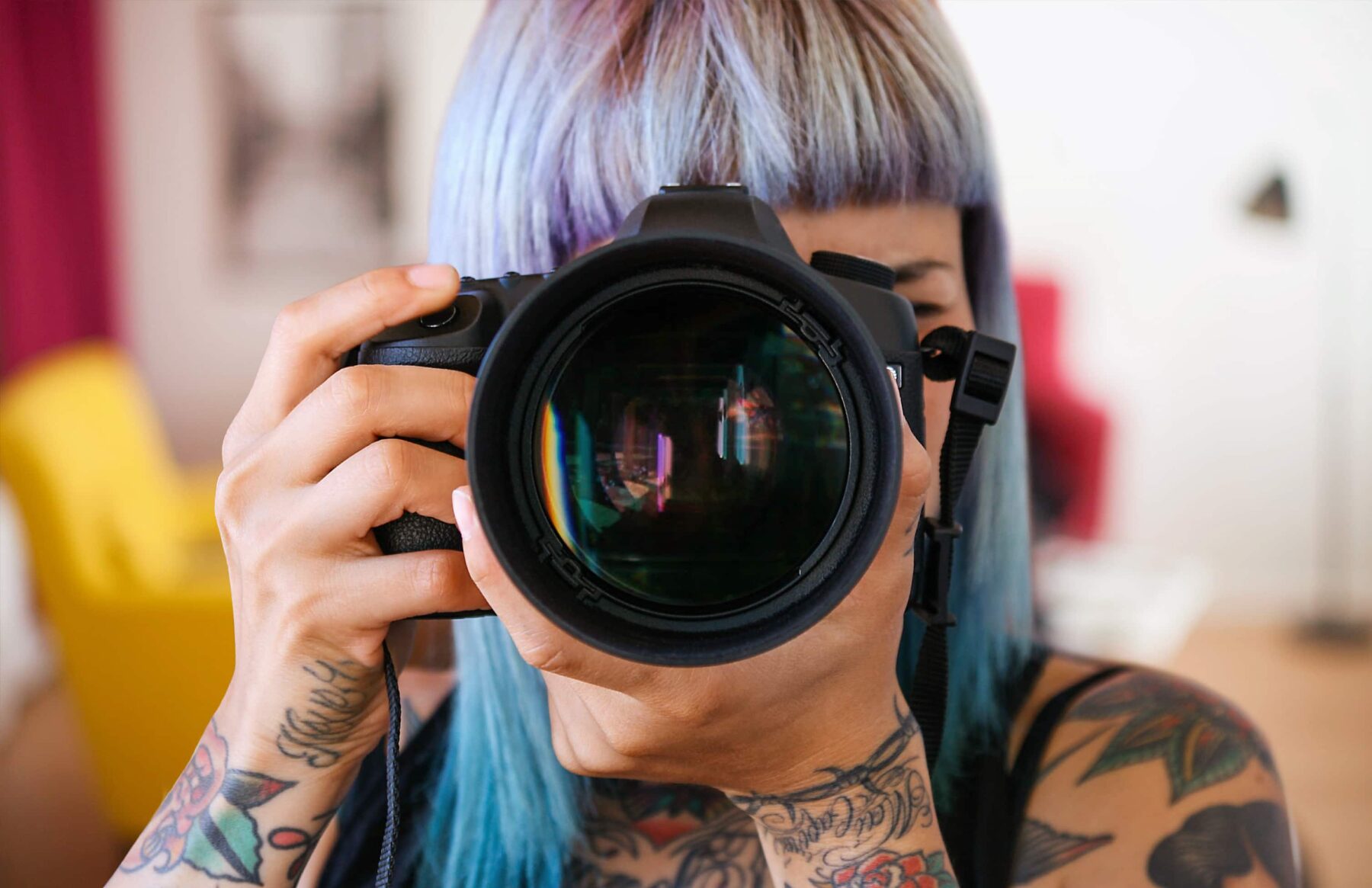 Woman with purple hair aiming a camera directly at the viewer