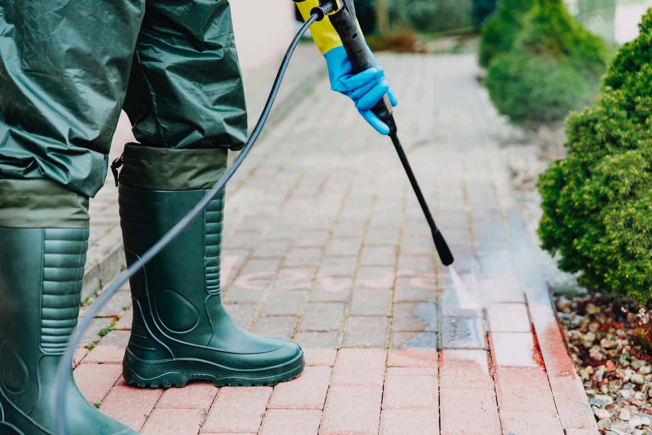 Man cleaning red, conrete pavement block using high pressure water cleaner.