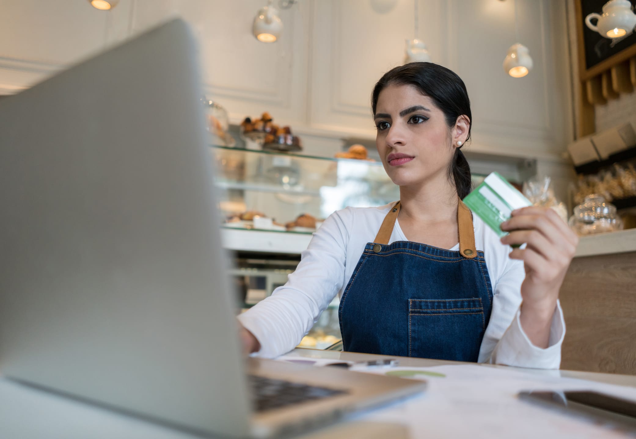 Serious female business owner of a bakery shopping online with her credit card using her laptop.