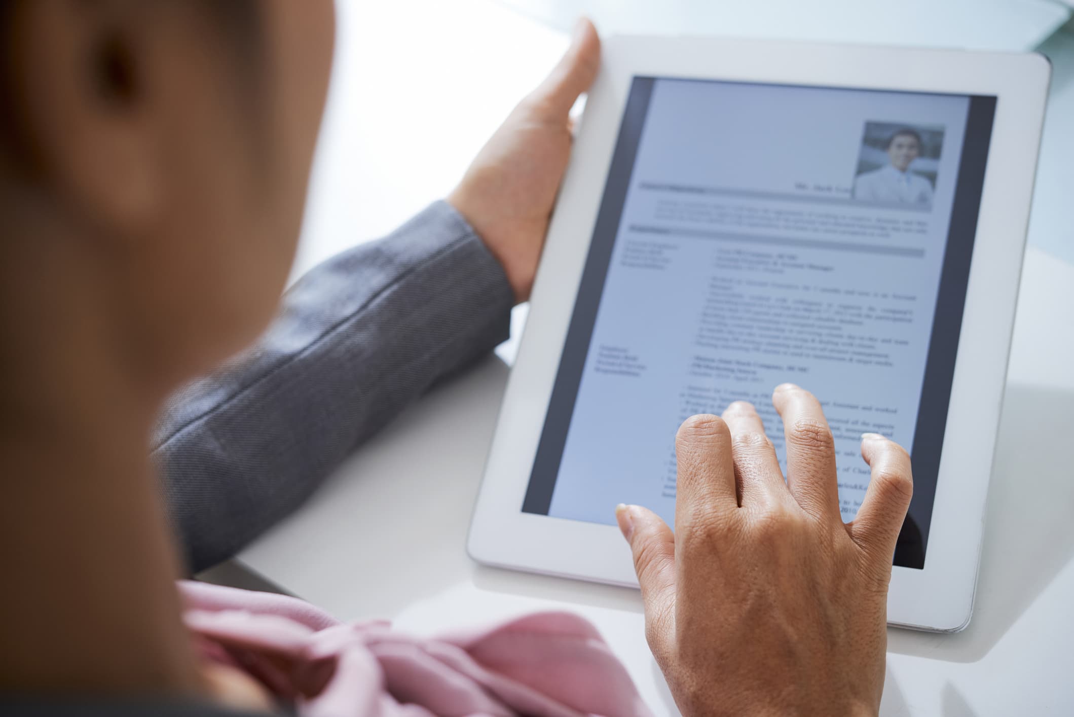 Hand of employer scrolling in touchpad while looking through information about an applicant in electronic resume.