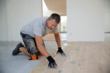 middle-aged man with gray hair glues, lays parquet floor