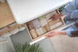 Top view of woman hands neatly organizing bathroom amenities and toiletries in drawer or cupboard in bathroom. Concept of tidying up a bathroom storage by using Japanese method.