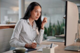 Woman seated at a computer, concentrating and taking notes